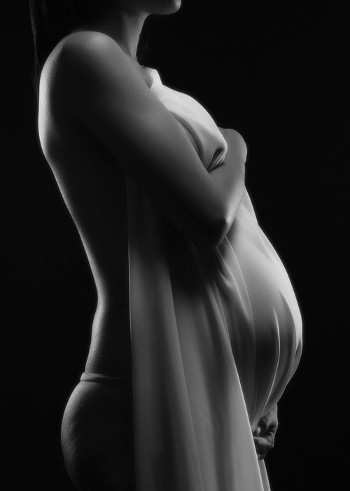 Fotografia de mulher grávida com um lençol sobre a barriga dela