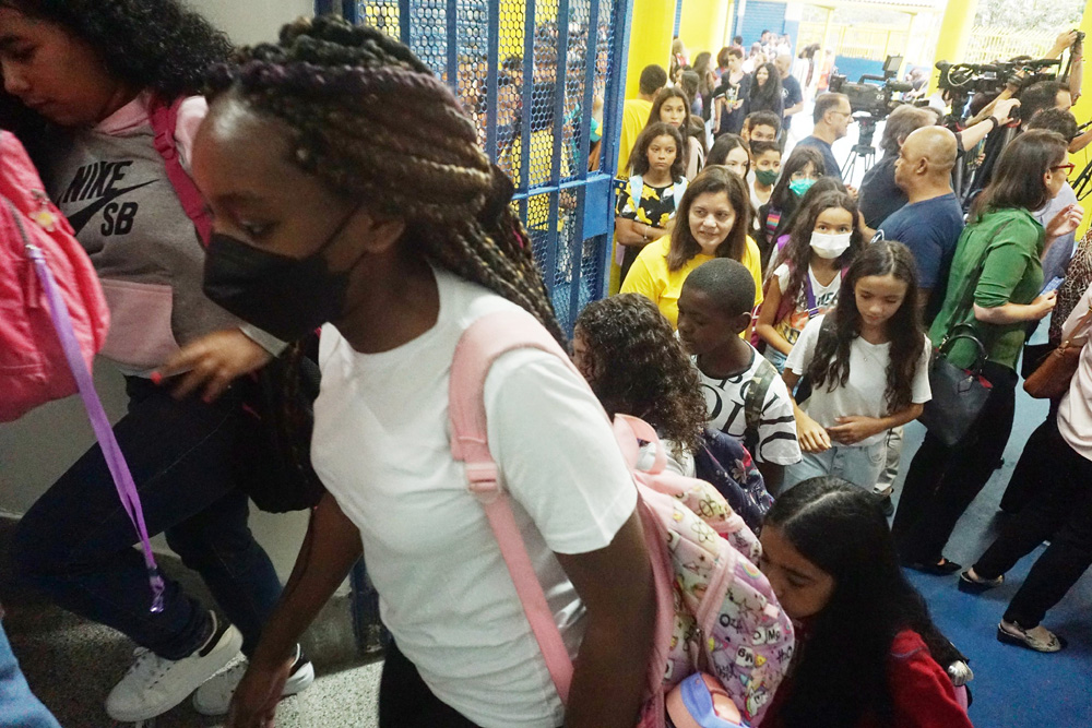 Crianças entrando na escola. A imagem destaca uma jovem estudante negra, usando uma máscara preta e uma mochila de cor rosa estampada. Crianças entrando na escola. A imagem destaca uma jovem estudante negra, usando uma máscara preta e uma mochila de cor rosa estampada.