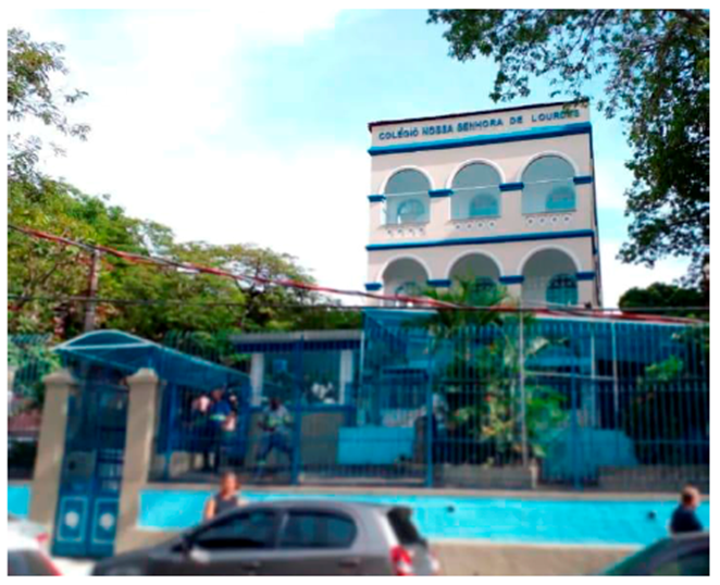 Fachada da Escola Nossa Senhora de Lourdes, no Rio de Janeiro. Em frente à escola, há alguns carros estacionados e algumas pessoas. Fachada da Escola Nossa Senhora de Lourdes, no Rio de Janeiro. Em frente à escola, há alguns carros estacionados e algumas pessoas.