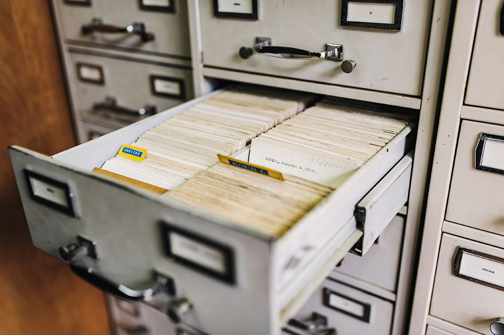 Gaveta de arquivo aberta com fichas organizadas e separadas por abas visíveis, mostrando uma disposição ordenada de documentos. Gaveta de arquivo aberta com fichas organizadas e separadas por abas visíveis, mostrando uma disposição ordenada de documentos.