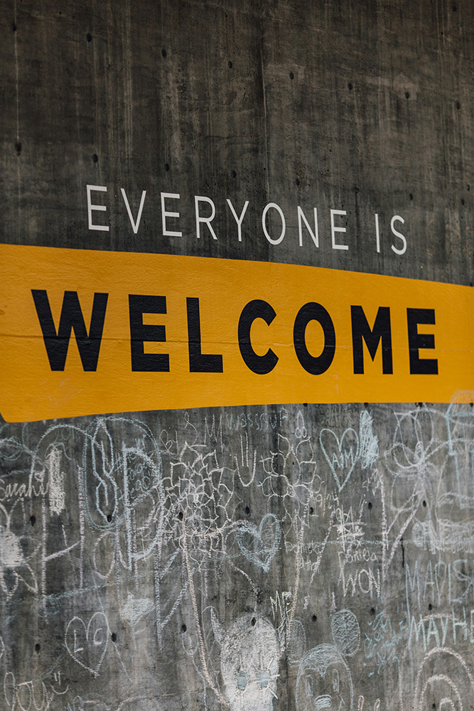 Fotografia de uma parede cinza com um mural onde se lê "Everyone is welcome" Fotografia de uma parede cinza com um mural onde se lê "Everyone is welcome"
