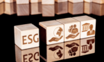 Imagem digital de blocos de madeira enfileirados. Da esquerda para a direita, no primeiro bloco se lê "ESG", no segundo bloco há uma ilustração do planeta Terra apoiado por uma mão, no terceiro bloco se vê a ilustração de bonecos representando pessoas apoiados por uma mão e no quarto se vê um boneco à frente de um prédio com colunas gregas.