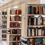 Fotografia de um corredor claro de uma biblioteca com diversas estantes com livros.