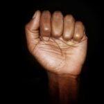 Fotografia de uma mão de pele negra fechada em punho em um fundo preto
