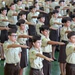 Fotografia de crianças com uniformes de escola militar e com um dos braços esticados para frente